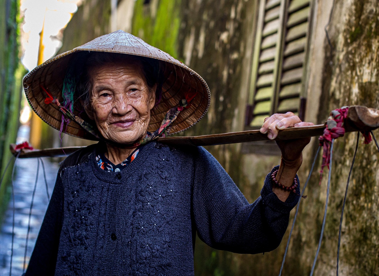 Older Vietnamese woman wearing a conical hat and carrying a shoulder pole